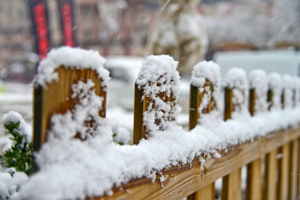 An image showing snow and ice that have collected on a wooden, picket-style fence.