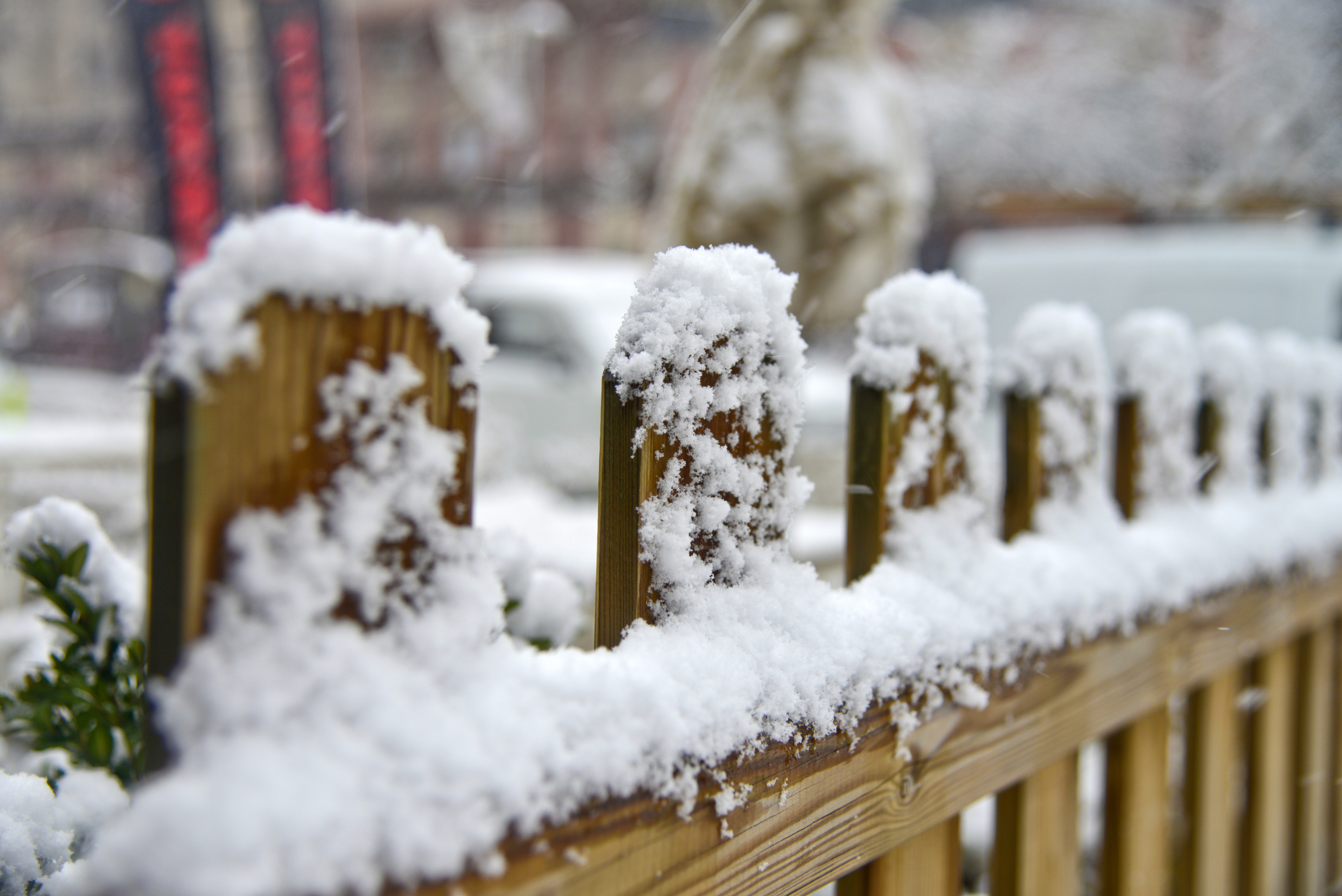 An image showing snow and ice that have collected on a wooden, picket-style fence. 
