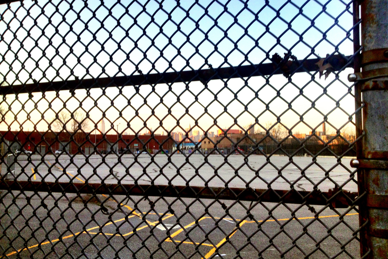 A chain length fence at a business/industrial area in either the early morning or late afternoon. High-rise buildings can be seen in the distant background.