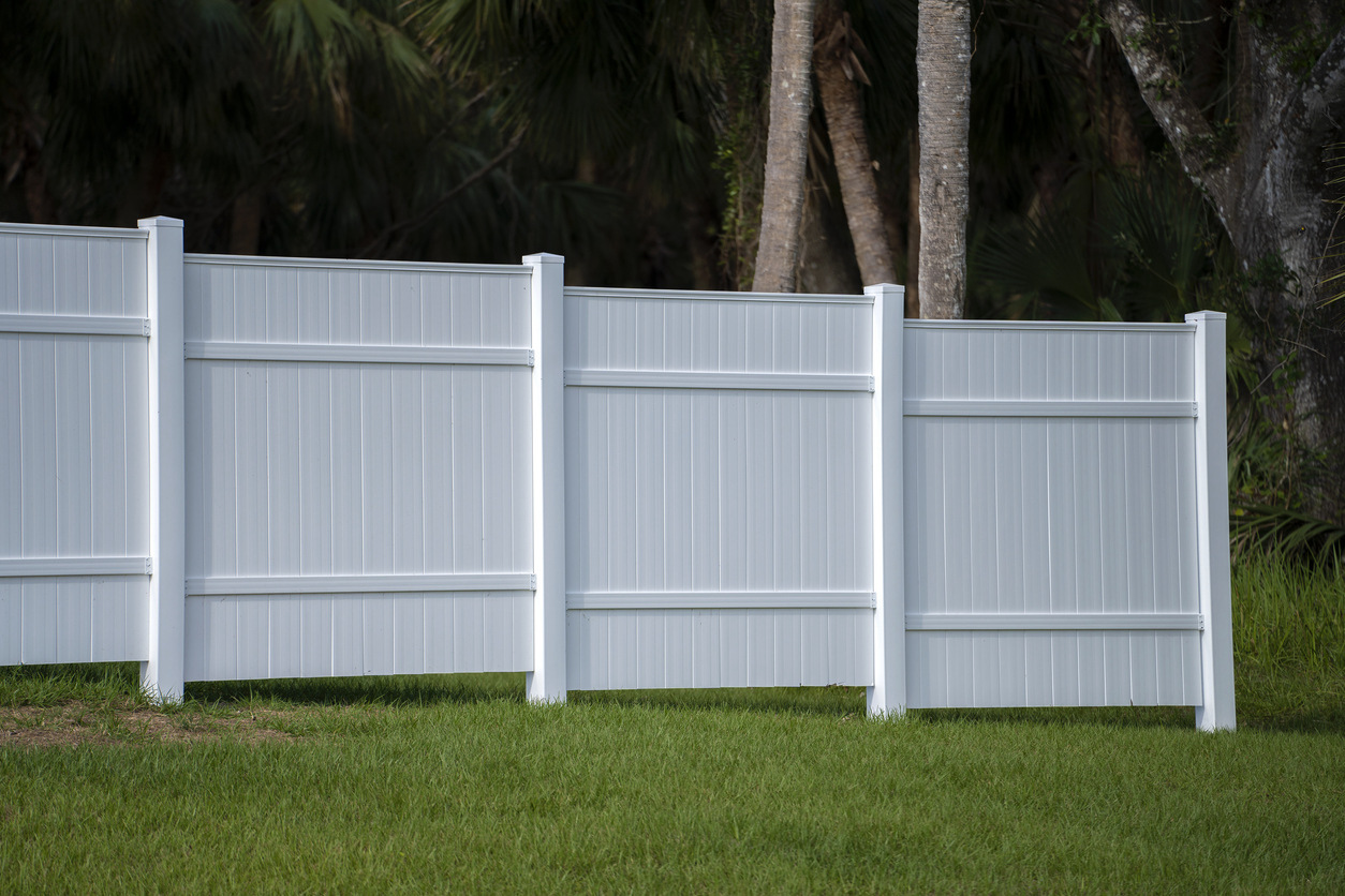 A beautiful white vinyl fence bordering a green backyard, providing privacy for the honeowners.