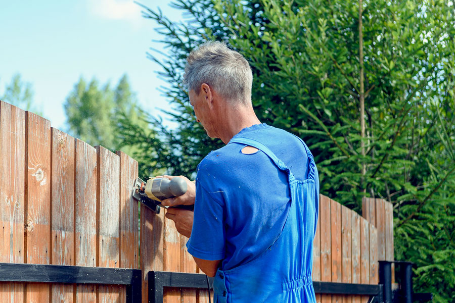 Man in blue repairing wooden fence in Glenview